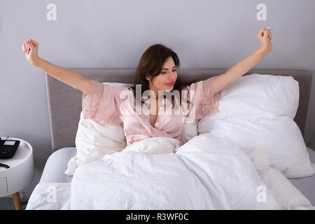 Belle jeune femme s'étendant ses bras sur le lit dans la chambre Banque D'Images