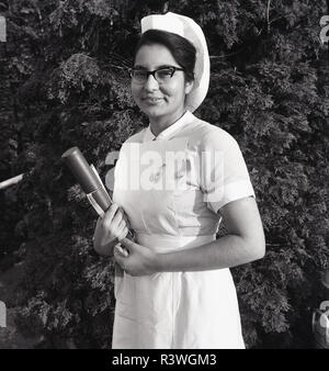 1965, la Grande-Bretagne, NHS,une infirmière à l'étranger fier du sous-continent indien à l'extérieur dans son uniforme tenant son British Royal College de Nursiing (MRC) qualifications et portant un boa watch et de soins infirmiers, l'insigne de qualification de l'Angleterre, Royaume-Uni. Banque D'Images