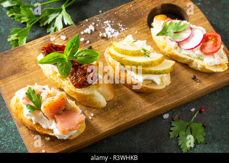 En-cas d'Antipasti close-up set pour le vin. Variété Brushetta avec fromage doux, de poire, de radis, de saumon et tomates séchées servi sur une planche en bois rustique sur Banque D'Images