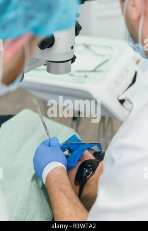 Médecin utilisé microscope. Dentiste est de traiter le patient en cabinet dentaire moderne. L'opération est réalisée à l'aide de batardeau. Client est inséré et restauré Banque D'Images