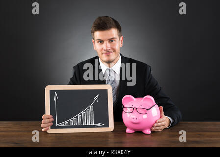 Businessman With Piggybank et tableau noir montrant Graphique Banque D'Images