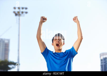 Jeune athlète masculin asiatique célébrant la victoire avec poings et bras levés Banque D'Images