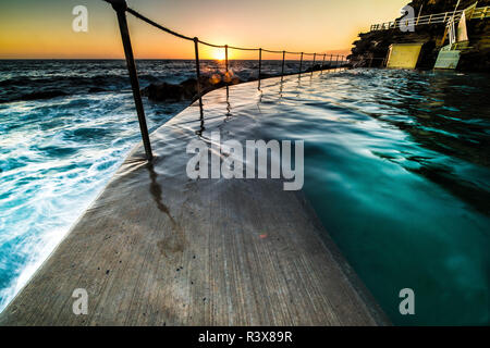 Piscine de Bronte, Sydney au lever du soleil à l'orb du soleil juste apparaître à l'horizon éclairant la roche piscine comme il avance dans l'océan Banque D'Images