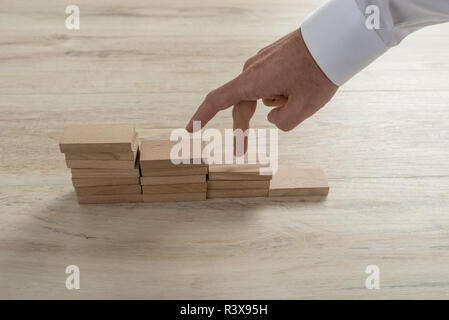 La main des hommes en chemise blanche balade ses doigts dans un escalier fait de blocs de bois. Banque D'Images