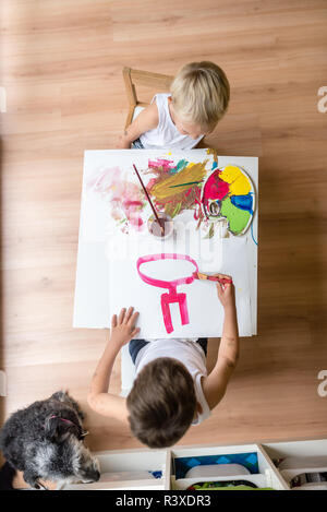 Portrait de deux enfants peinture sur petite table blanche avec chien assis sur le plancher. Banque D'Images