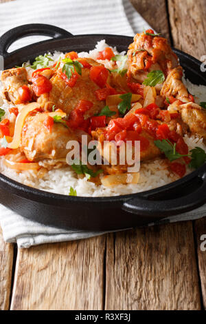Poulet haïtien dans une sauce tomate épicée avec riz d'accompagnement close-up dans une casserole sur la table verticale. Banque D'Images