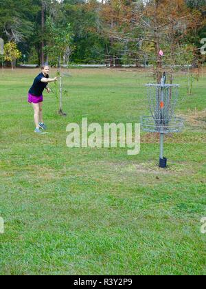 Mettre en place, athlétique jeune femme portant des shorts, jouer au disc golf dans un parc public, Gainesville, Alachua Comté, en Floride, aux États-Unis. Banque D'Images