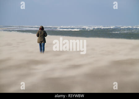 Woman walking on beach sur un jour de tempête en hiver, le sable soufflant sur la plage Banque D'Images