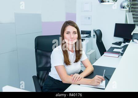 Portrait de gestionnaire administratif qualifié assis sur son bureau de travail et prendre des notes. Satisfait de l'occupation, les jeunes filles à la réception, par Banque D'Images