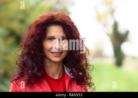 Girl in red sport suit smiling in garden. de long cheveux rouges et caractéristiques du Moyen-Orient Banque D'Images