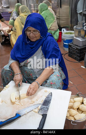 Une femme sikh dans une cuisine commune langar, trancher les pommes de terre pour distribuer de repas gratuits. Dans un temple dans le Queens, New York. Banque D'Images