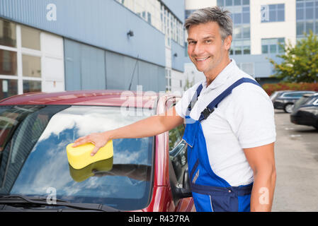 Heureux Travailleur homme pare-brise de voiture Nettoyage avec éponge Banque D'Images