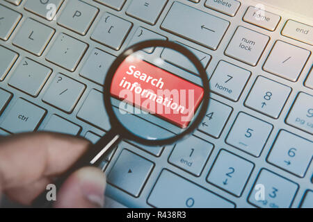 Recherche d'informations sur le bouton du clavier de l'ordinateur portable vue à travers la loupe. L'homme détient la loupe au-dessus de l'ordinateur clavier avec la touche rouge recherchez. Concept d'utiliser les moteurs de recherche en ligne. Banque D'Images