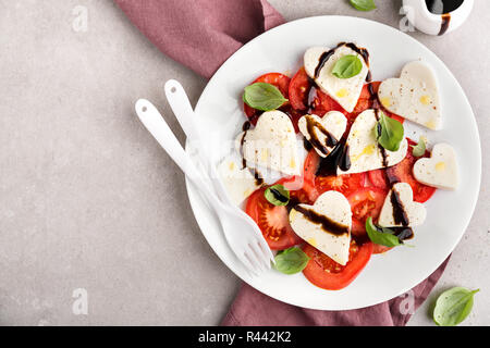 Saint-valentin salade. Salade caprese classique italien avec coeur formé de la mozzarella, basilic, tomates et balsamique servi sur assiette. Vue ci-dessus. Spa de copie Banque D'Images