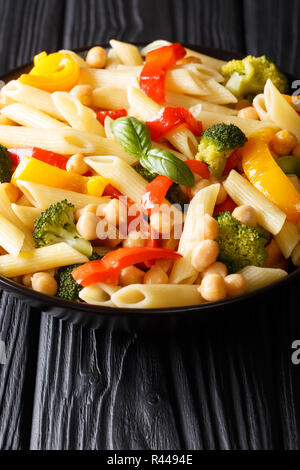 Pâtes penne avec les pois chiches, le brocoli, le poivron et les épices close-up dans une assiette sur la table verticale. Banque D'Images