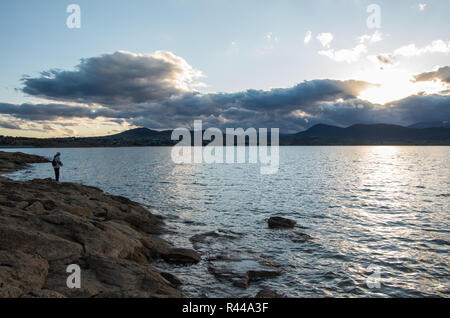 Au bord d'un pêcheur au coucher du soleil à Jindabyne dans l'arrière-plan Banque D'Images