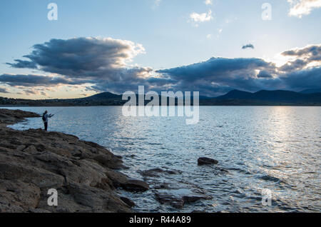 Au bord d'un pêcheur au coucher du soleil à Jindabyne dans l'arrière-plan Banque D'Images