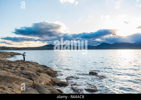 Au bord d'un pêcheur au coucher du soleil à Jindabyne dans l'arrière-plan Banque D'Images