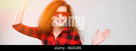 Jeune fille rousse dans une chemise à carreaux rouge. Charmante Jeune fille en rouge lunettes. Young Girl Dancing Banque D'Images