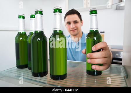 Smiling Man dépose une bouteille de bière du réfrigérateur Banque D'Images