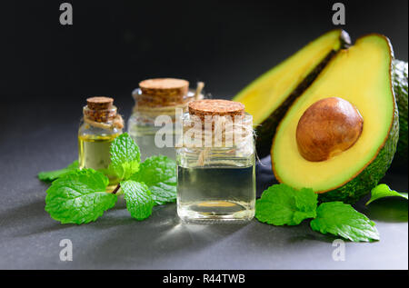 L'huile d'avocat et les rondelles d'avocat frais sur fond noir en noir. Huile cosmétique bio concept Banque D'Images