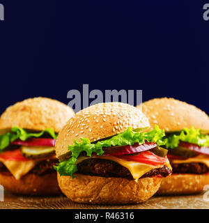 Trois des hamburgers avec du boeuf, tomate, cornichon, fromage, les oignons et la laitue sur fond de bois. De savoureux plats maison close up Banque D'Images