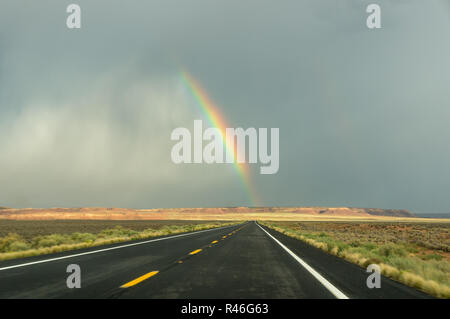 Fin d'un arc-en-ciel sur un fond noir une route après de fortes pluies Banque D'Images