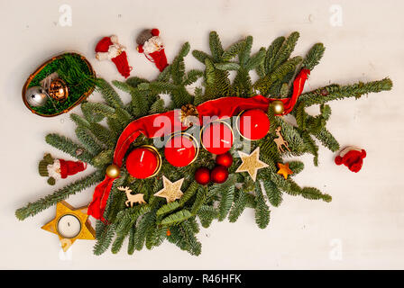 Une couronne avec quatre bougies rouges sur une branche de sapin entouré de décoration de Noël sur un tableau blanc Banque D'Images