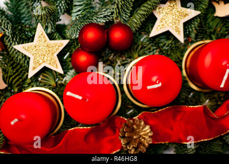 Une couronne avec quatre bougies rouges sur une branche de sapin entouré de décoration de Noël sur un tableau blanc Banque D'Images