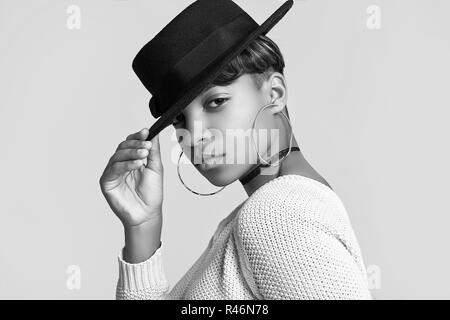 Portrait de jeune belle fille noire hipster avec les cheveux courts en blanc et pull fashion hat isolé sur fond blanc. Shoot Studio. Banque D'Images