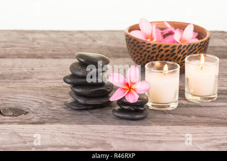 Plumeria fleurs, pierres noires et les bougies sur fond de bois patiné Banque D'Images