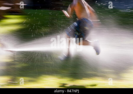 Jeune garçon passe par des sprinkleurs dans le soleil d'été Banque D'Images