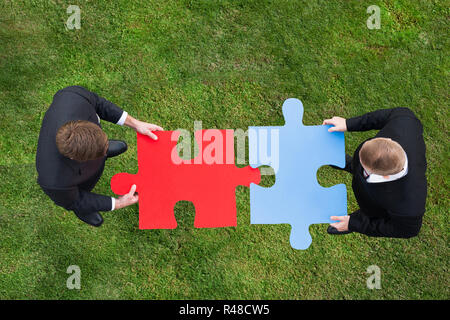 Les hommes d'adhérer à des pièces de puzzle en se tenant sur le terrain herbeux Banque D'Images