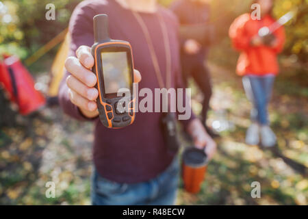 Photo de l'homme tenant le téléphone satellite et thermocup en mains. Il montre à la caméra. Jeune homme et femme se tenir derrière. Banque D'Images