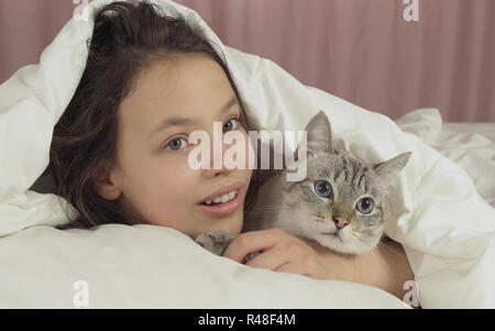 Happy teen girl baisers et des pourparlers avec Thai cat in bed Banque D'Images