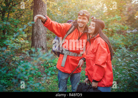 Jeune homme positif se trouve à proximité femme et pointe vers l'avant. Elle se penche vers lui. Ils sourient ensemble. Les gens sont en vert forêt. Banque D'Images