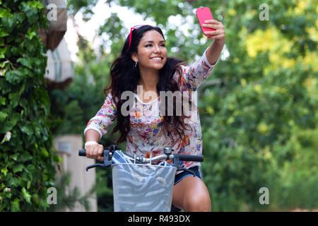 Pretty young girl riding bike et en tenant un. selfies Banque D'Images