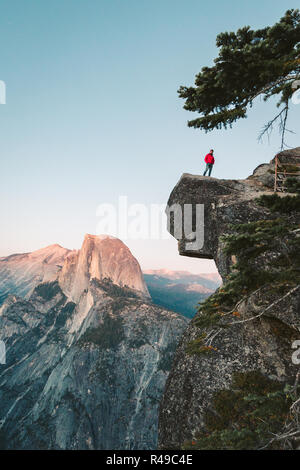 L'intrépide randonneur est debout sur un rocher en surplomb en profitant de la vue vers célèbre Demi Dôme à Glacier Point oublier dans beau crépuscule du soir Banque D'Images