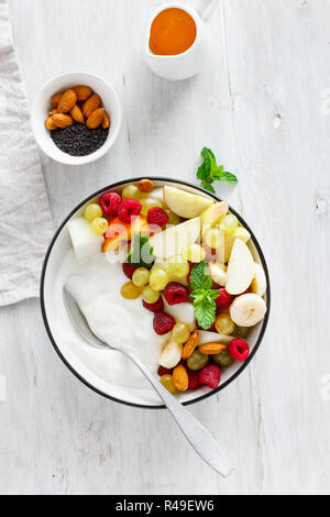 Petit-déjeuner sain bol : yaourt nature et de fruits (raisin, pomme, framboise, menthe, pêche, banane) sur table en bois blanc Vue de dessus Banque D'Images