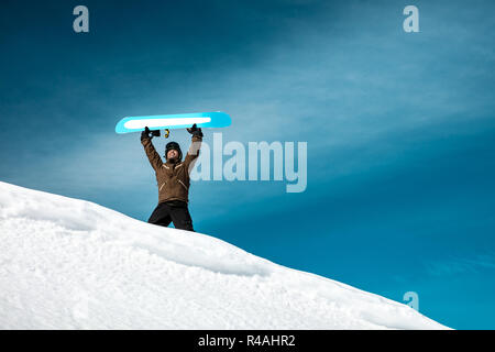 Homme heureux a soulevé une planche au-dessus de sa tête et se dresse sur le sommet d'une montagne contre le ciel bleu, des compétitions en sports d'hiver, d'été active vac Banque D'Images