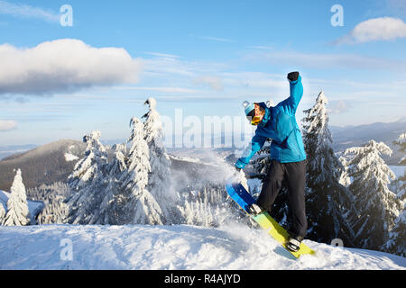 Snowboarder faisant des tours à ski resort. Rider saut de la scène avec son snowboard près de l'arrière-pays ou sur la forêt freeride freestyle session en mode coloré tenue. Copyspace domaine. En poudre dans l'air. Banque D'Images