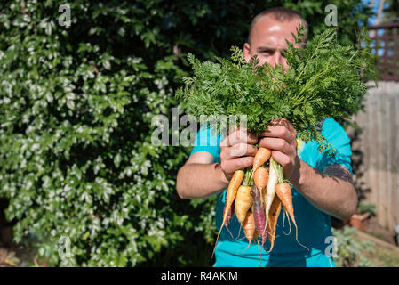 Un jeune homme de l'Australie blanche 21 ans holding up home grown légumes anciens carottes dans une arrière cour jardin Banque D'Images