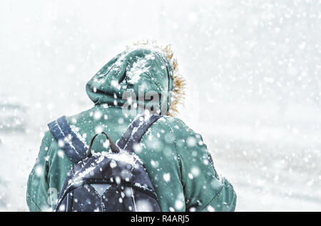 Vue arrière de l'homme en veste verte avec sac à dos dans le capot en blizzard. Chutes de neige. Arrière-plan de mauvais temps d'hiver Banque D'Images