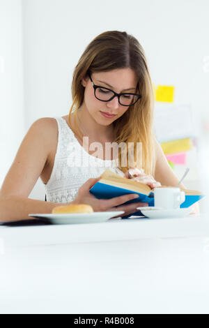 Jolie Jeune femme lisant un livre et le petit-déjeuner à la maison. Banque D'Images