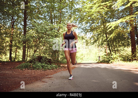 Jeune femme blonde sportive en short et un tanktop court seul le long chemin forestier sur une journée ensoleillée Banque D'Images