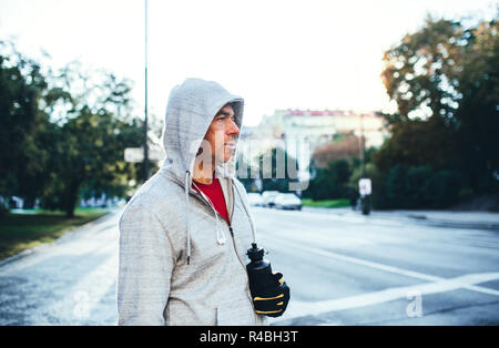 Mâle mature runner avec de l'eau bouteille debout à l'extérieur en ville, se reposer. Banque D'Images