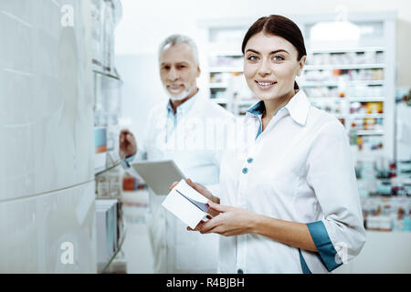 Mettre en ordre. Heureux brunette tenue pharmacien sourire sur son visage tout en démontrant des nouveaux médicaments Banque D'Images