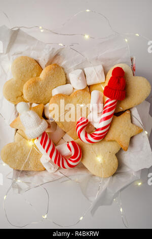 Composition de Noël. Boîte-cadeau avec des biscuits de Noël, des cannes de bonbon et un décor amusant, la guirlande de lumière sur fond blanc. Mise à plat, vue du dessus Banque D'Images