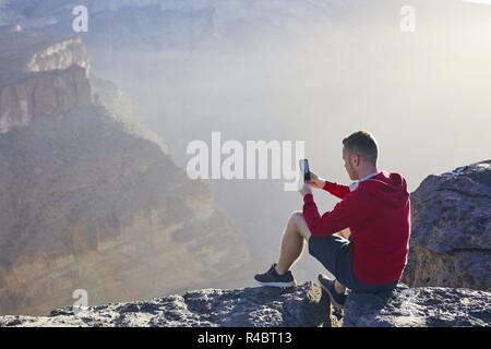 Détente dans les montagnes. Jeune homme photographié par téléphone mobile. Le Jebel Akhdar, Grand Canyon d'Oman. Banque D'Images