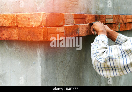 L'installation sur le mur de briques et des travailleurs et travailleuses de mains d'installer des briques rouges avec du ciment plâtre sur le site de construction Banque D'Images